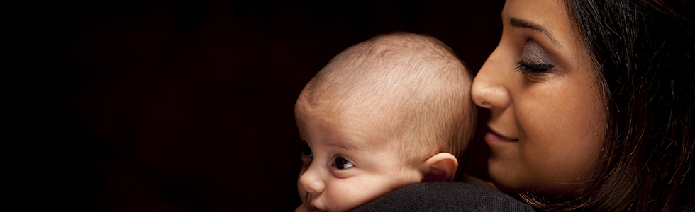 Young Attractive Ethnic Woman Holding Her Newborn Baby Under Dramatic Lighting.